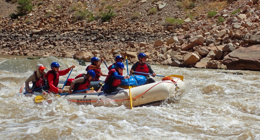 A group of students paddle a raft through whitewater.